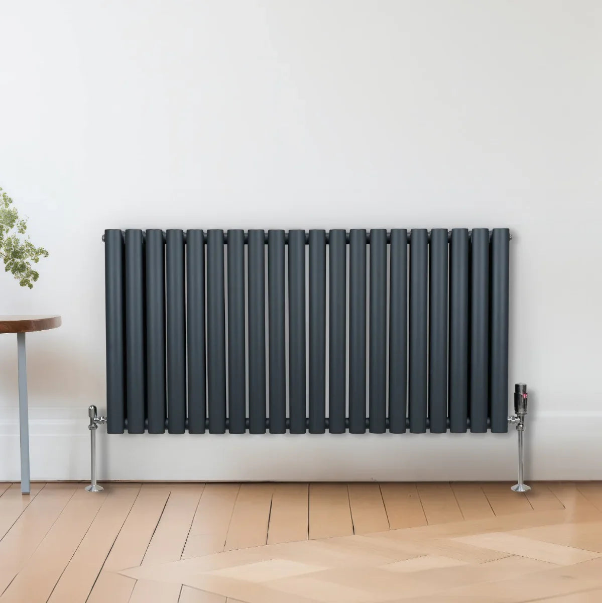 Oval column radiator in anthracite grey, featuring sleek, vertical tubes and a modern design, mounted on a wooden floor