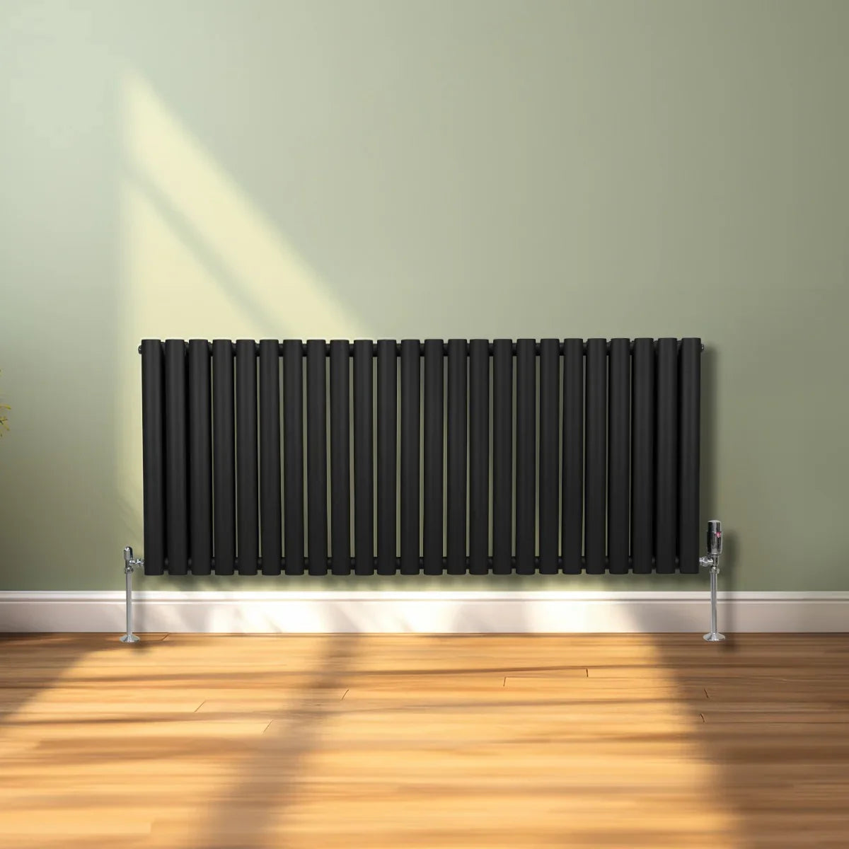 Sleek black oval column radiator, 600mm x 1440mm, mounted against a light green wall, with silver feet on a wooden floor
