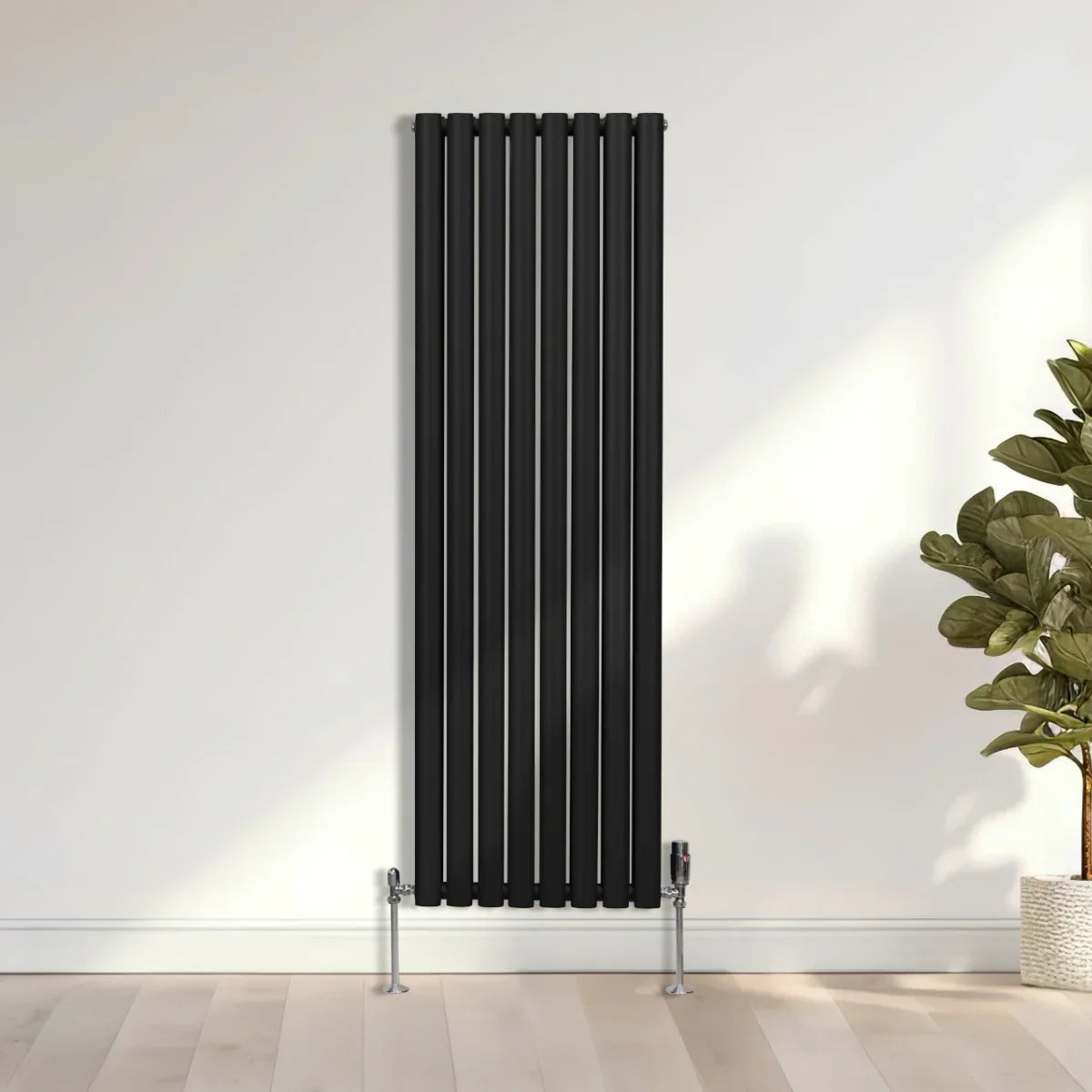 Sleek black oval column radiator, 1600mm x 480mm, featuring vertical bars and modern design, mounted against a light wall with greenery nearby