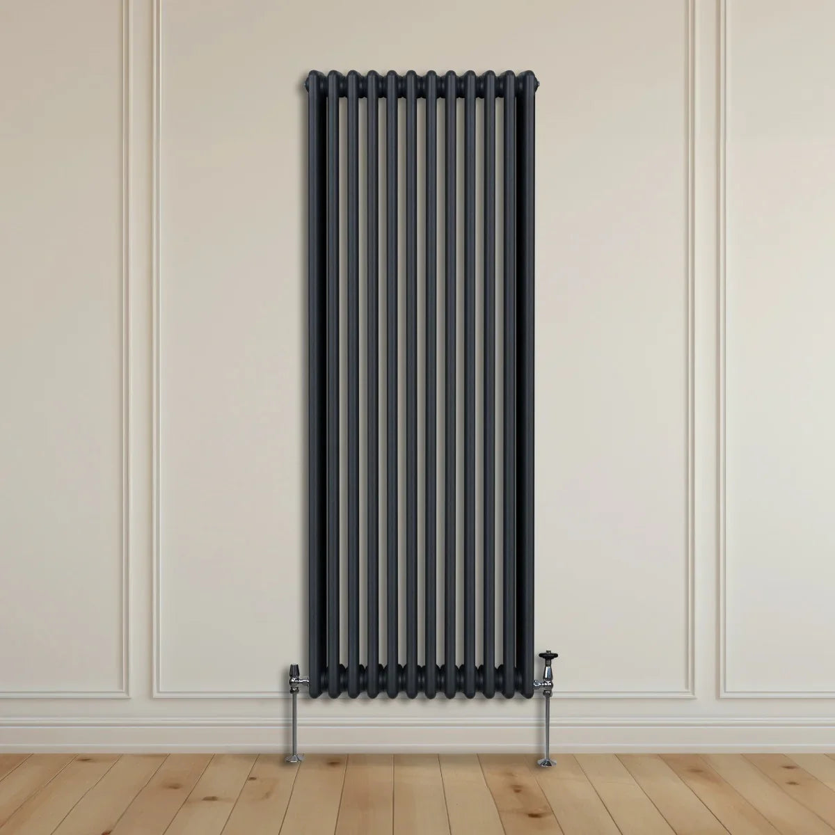 Traditional 3 column radiator in anthracite grey, featuring vertical bars and chrome feet, mounted on a light wooden floor against a neutral wall