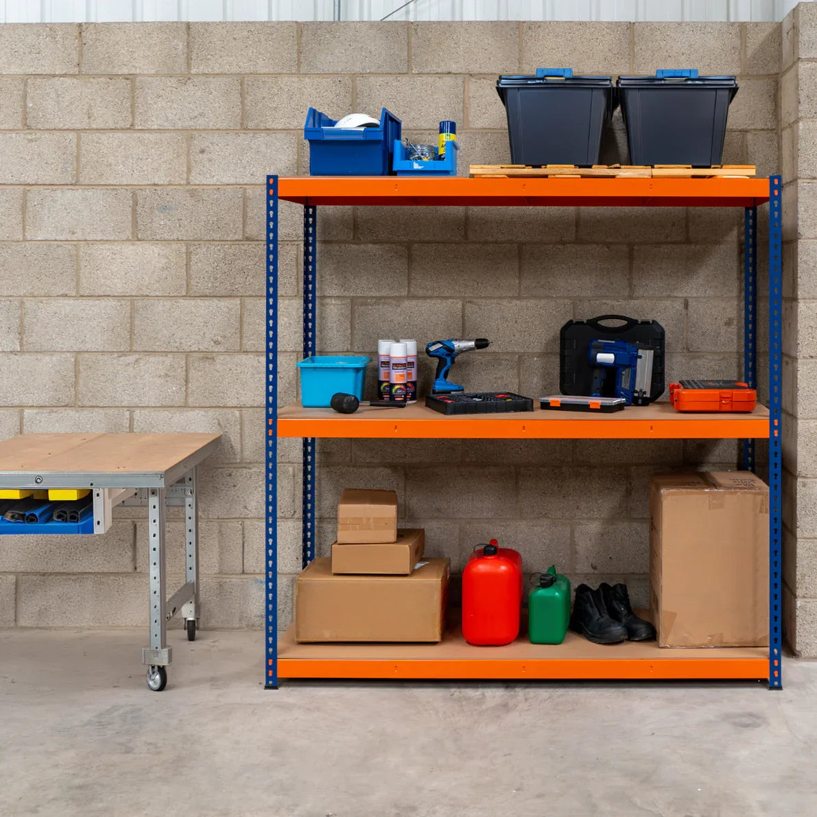 S-Rax 3 Shelf Racking in blue and orange, featuring tools, storage bins, and boxes organized on sturdy shelves against a concrete wall