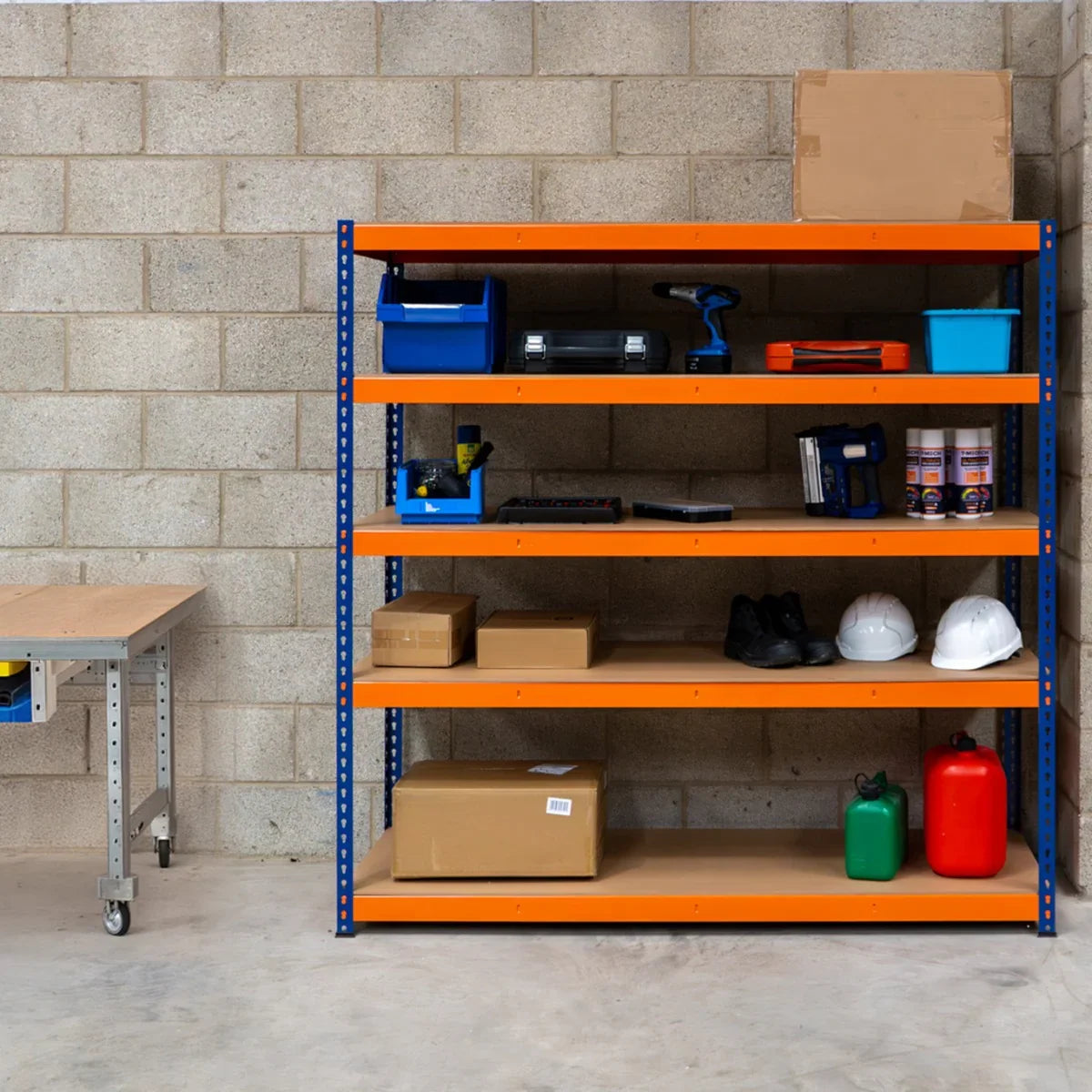 Five-shelf industrial racking unit with orange shelves and blue frame, holding tools, boxes, and safety gear in a garage setting