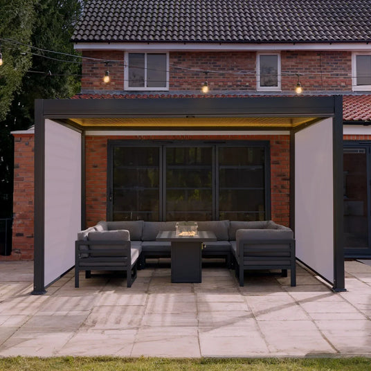Modern outdoor patio with a sleek black metal pergola, gray sectional sofa, and a glass-top coffee table, surrounded by greenery