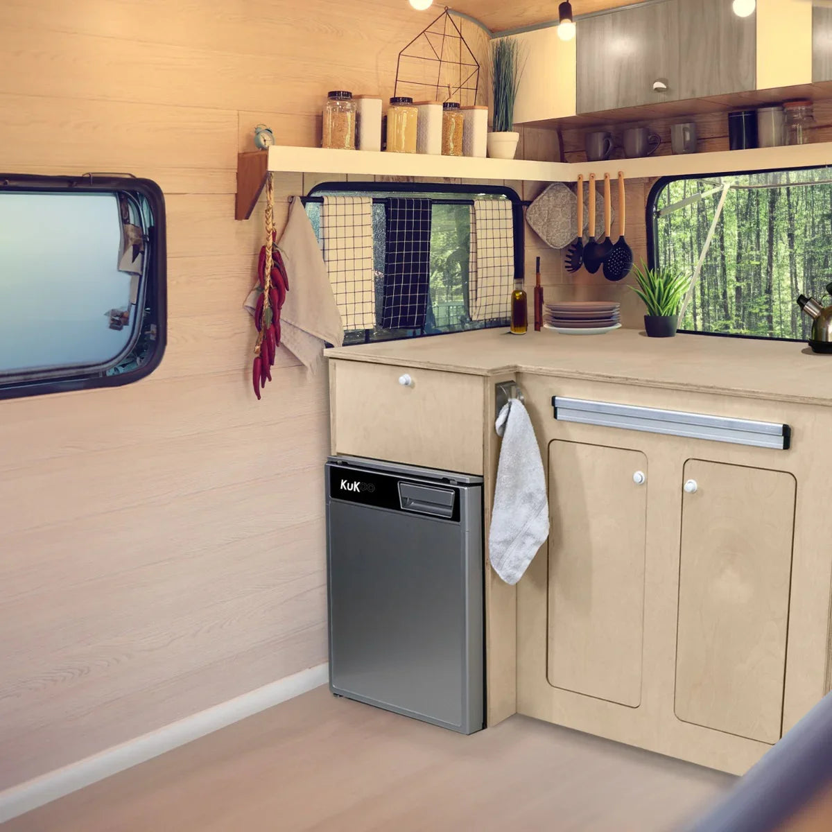 Stylish camper kitchen pod featuring a sleek silver compressor fridge, wooden cabinetry, and modern cooking accessories in a cozy interior