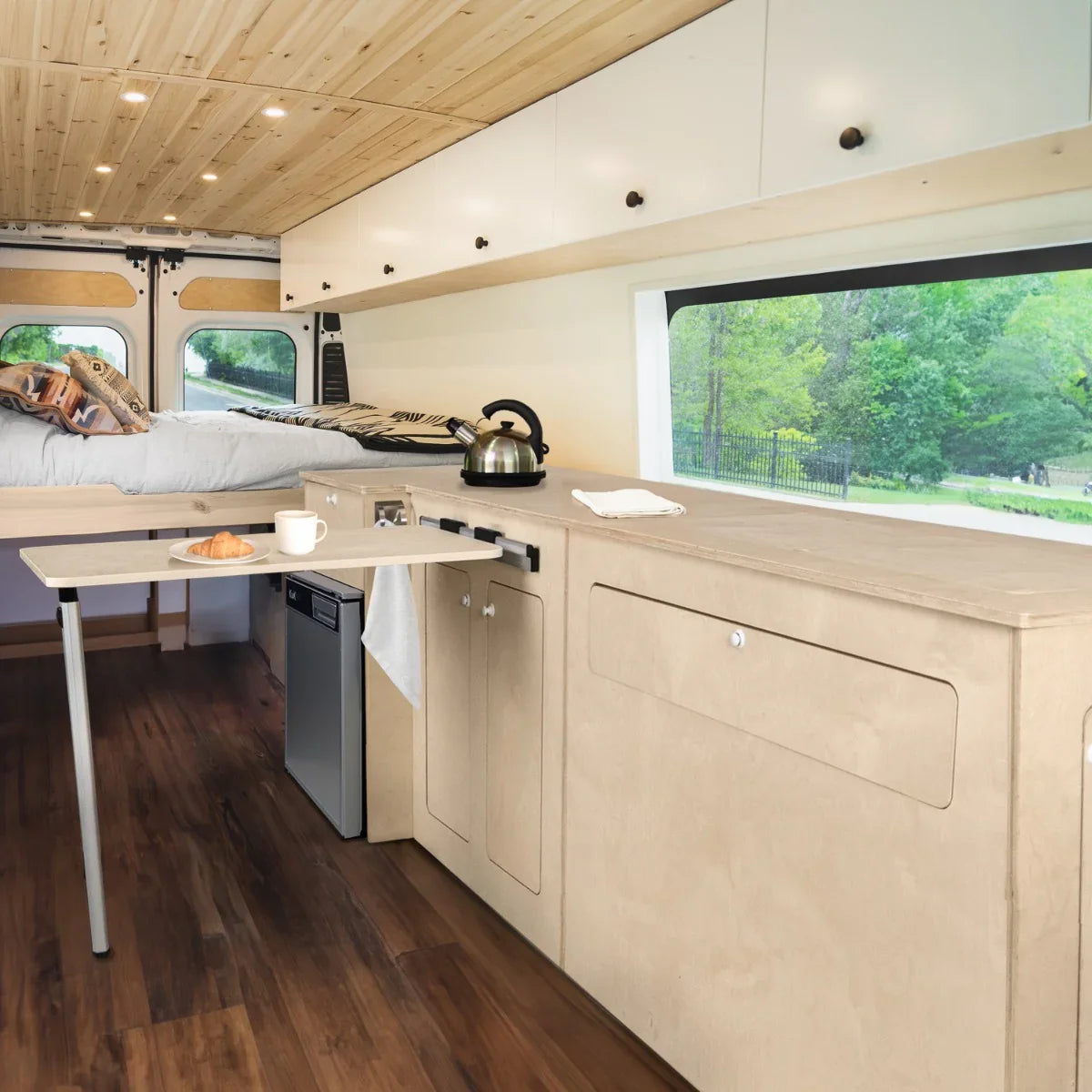 Camper Kitchen Pod with silver compressor fridge, light wood cabinetry, foldable table, and cozy interior with natural light