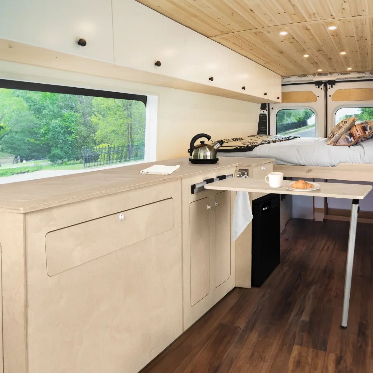 Camper kitchen pod with light wood cabinetry, black compressor fridge, and a cozy interior featuring a bed and dining table setup
