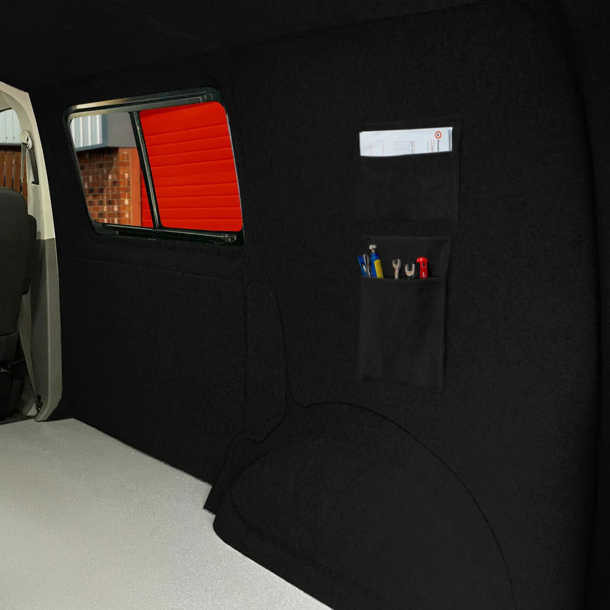 Black van carpet lining featuring storage pouches for tools, with a smooth texture and a sleek, seamless design against a dark interior