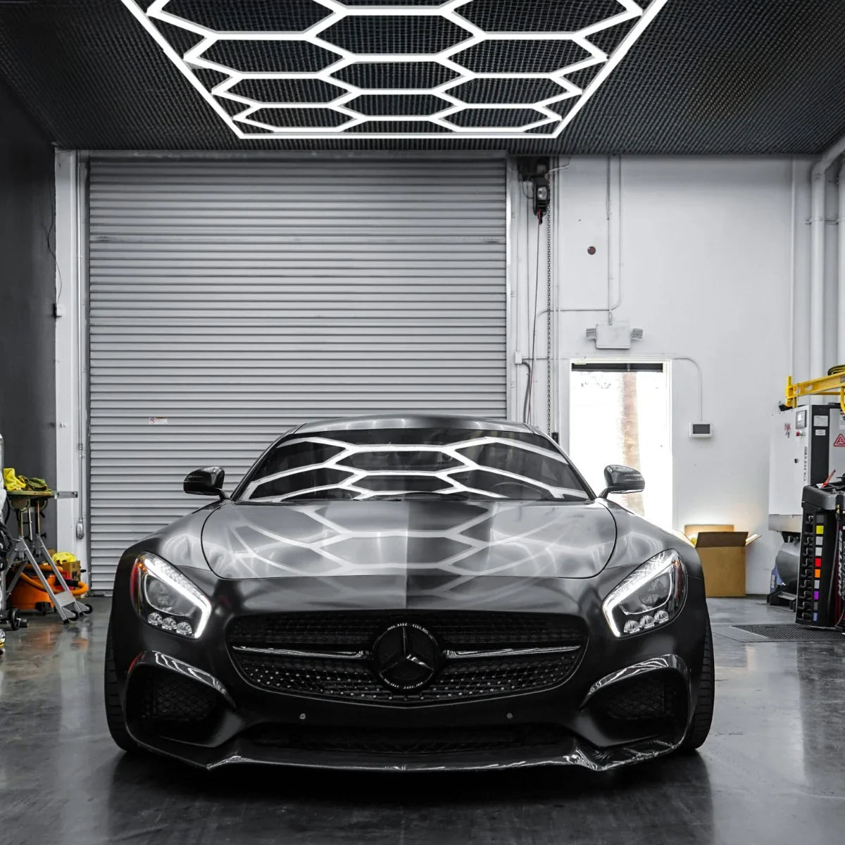 Hexagon LED lighting installation above a sleek black sports car in a modern garage, showcasing geometric patterns and bright illumination