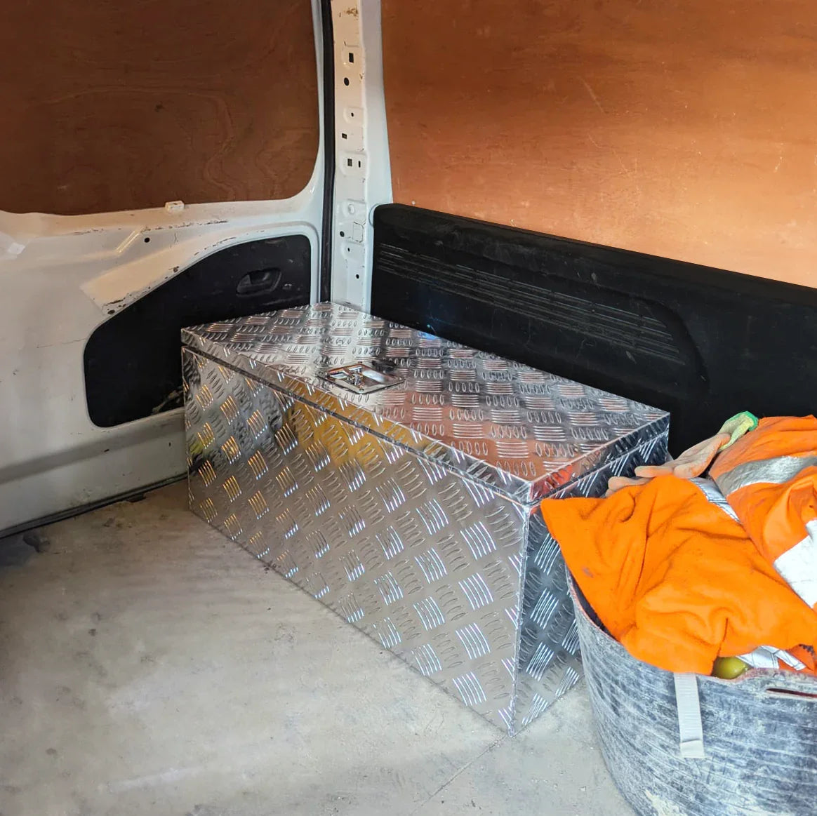 Large 70L aluminum tool box with a diamond plate texture, placed in a van, surrounded by a colorful blanket and storage bag