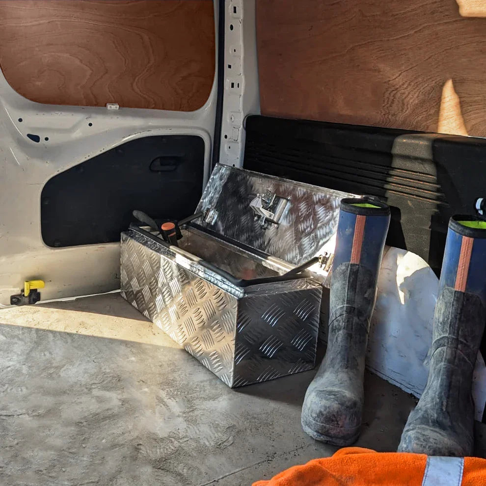 Aluminium tool box 60L with a diamond plate finish, placed inside a van beside rubber boots and an orange towel