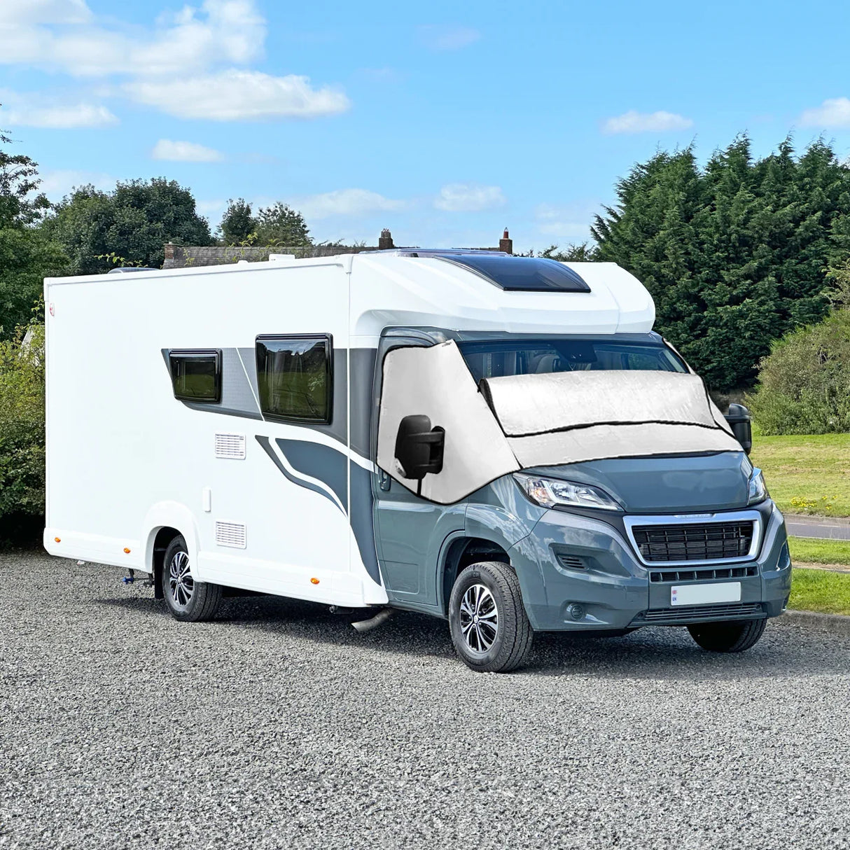 Motorhome screen cover in white, fitted on a gray motorhome, providing sun protection with a sleek design against a green landscape