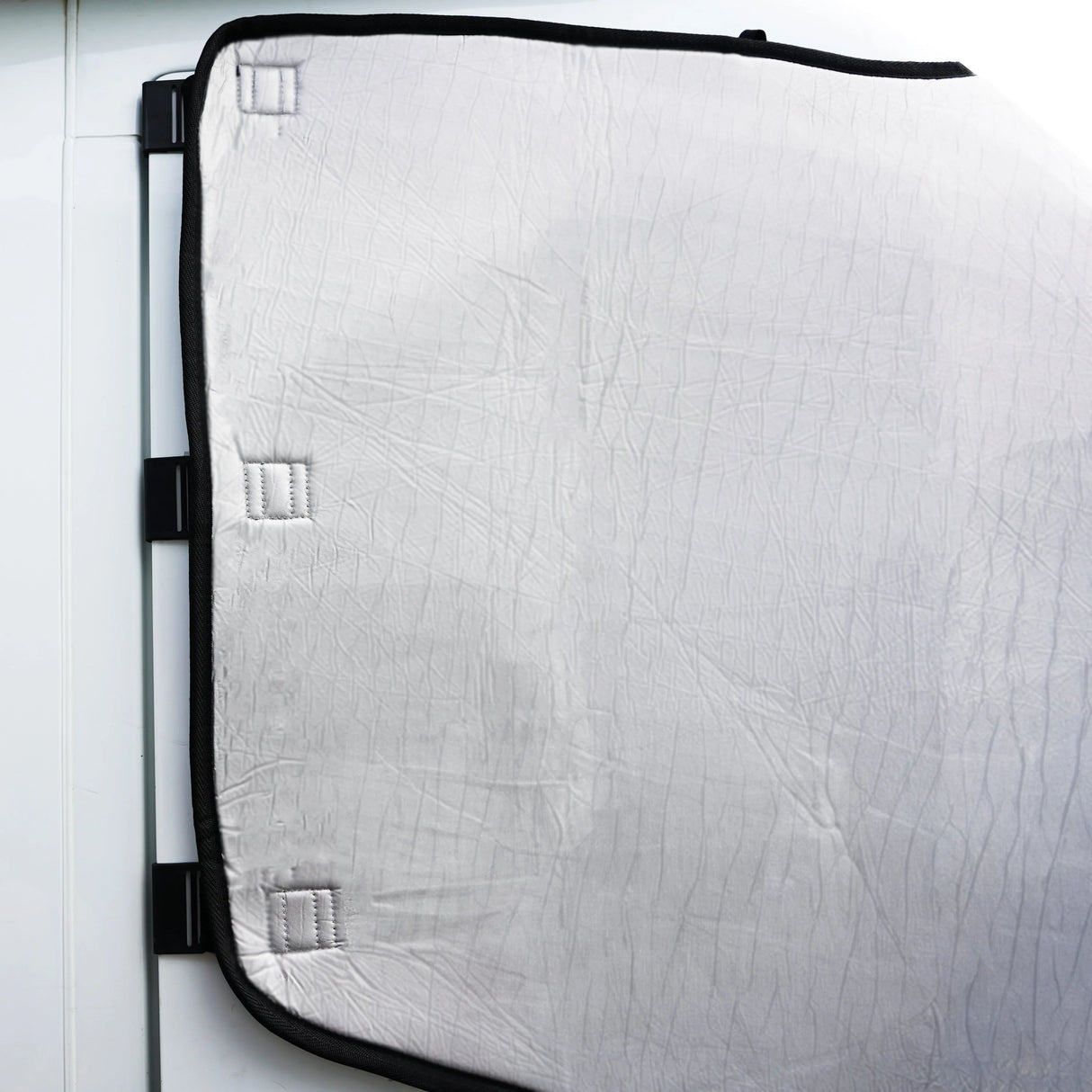 Motorhome screen cover in white with a textured surface, featuring black edges and secure attachment points for easy installation