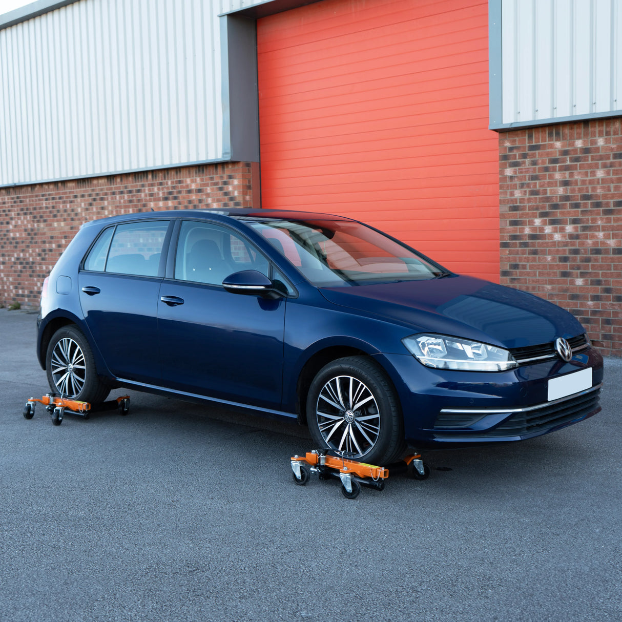 Hydraulic positioning skates in orange and black support a blue car, showcasing their sturdy wheels and low-profile design for easy maneuverability