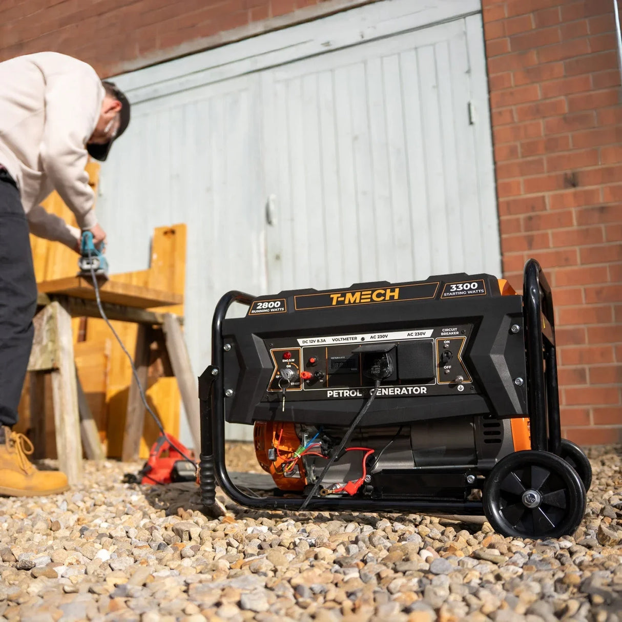 T-Mech portable petrol generator with a black and orange design, wheels for mobility, and control panel, set on gravel outdoors