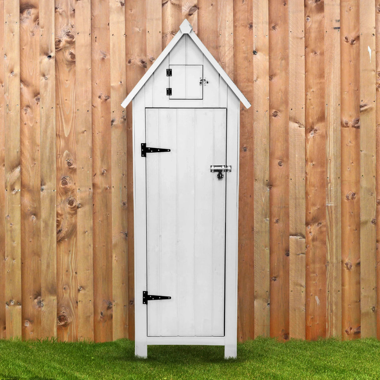 White wooden garden shed with a peaked roof, featuring a front door, small upper window, and black metal hardware against a wooden fence backdrop