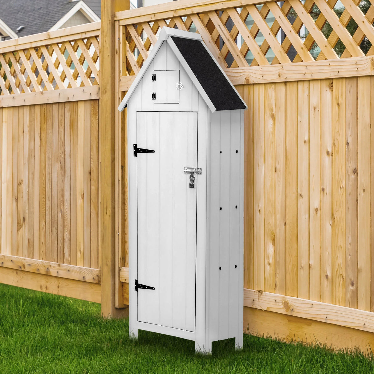 White wooden garden shed with a sloped roof, black shingles, and a sturdy door, set against a wooden fence and green grass