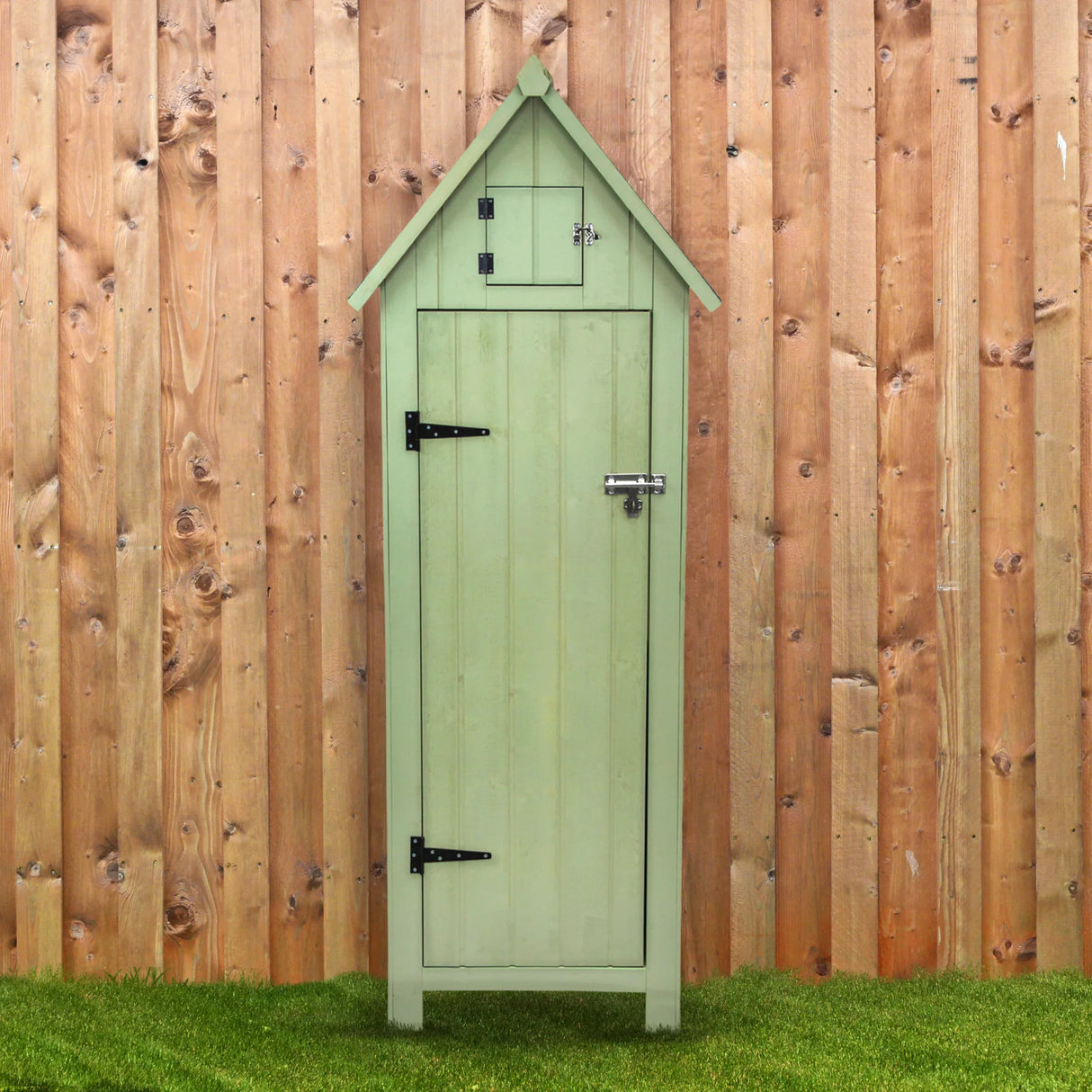Green wooden garden shed with a pointed roof, vertical slats, and a small top window, set against a wooden fence background