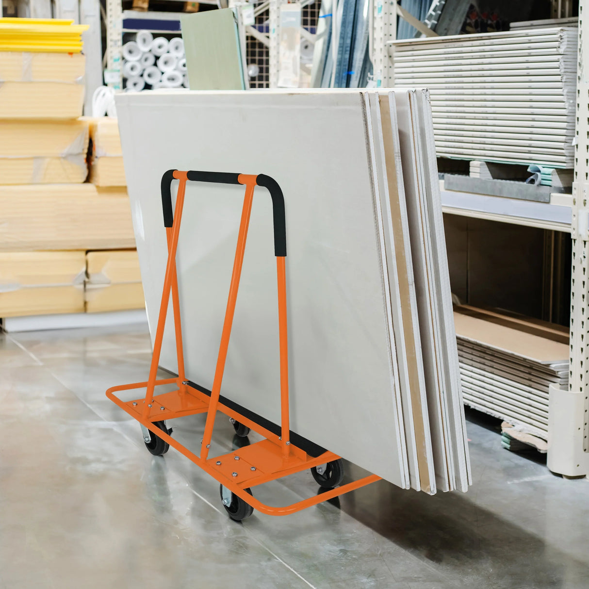 Dry wall cart with orange frame, holding multiple plasterboards, positioned in a storage area with building materials in the background