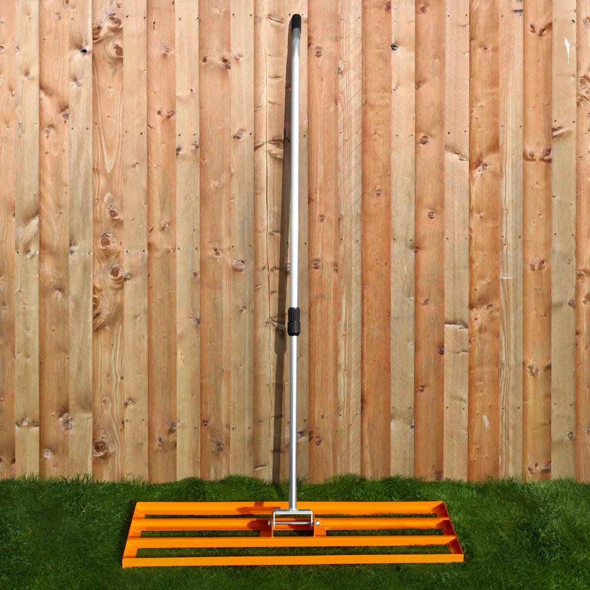 100cm orange lawn leveller and aerator with a sturdy metal handle, set against a wooden fence and grassy background