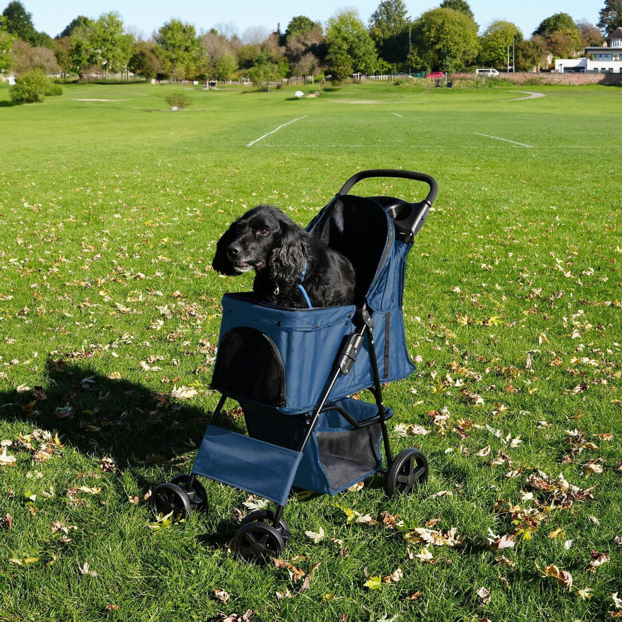 Navy blue pet stroller with rain cover, featuring a spacious mesh compartment and sturdy wheels, parked on a grassy field with a dog inside