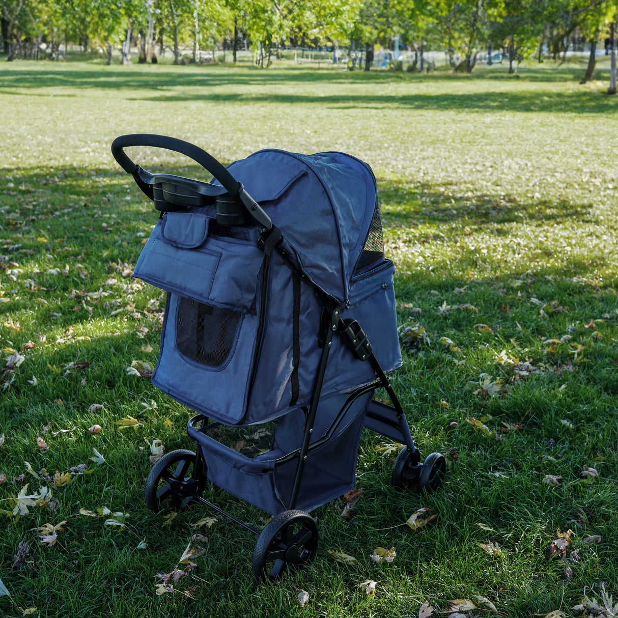 Navy blue pet stroller caddy bag with spacious compartments, mesh pockets, and sturdy wheels, set on green grass in a park