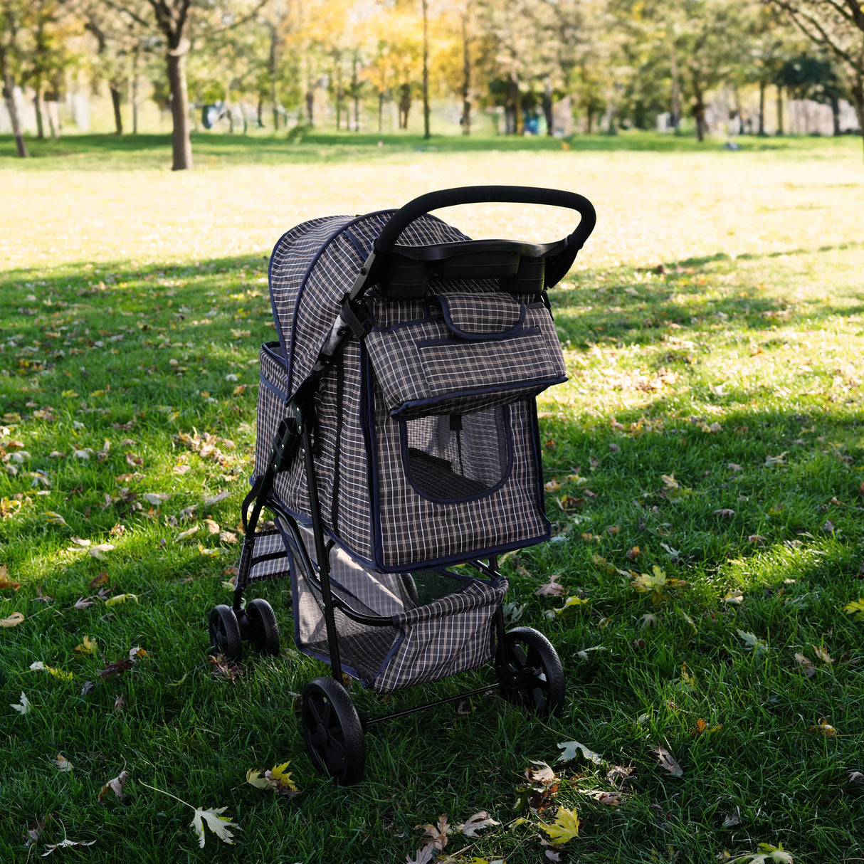 Pet stroller caddy bag in blue tartan pattern, featuring a spacious compartment, mesh windows, and sturdy wheels, set in a park