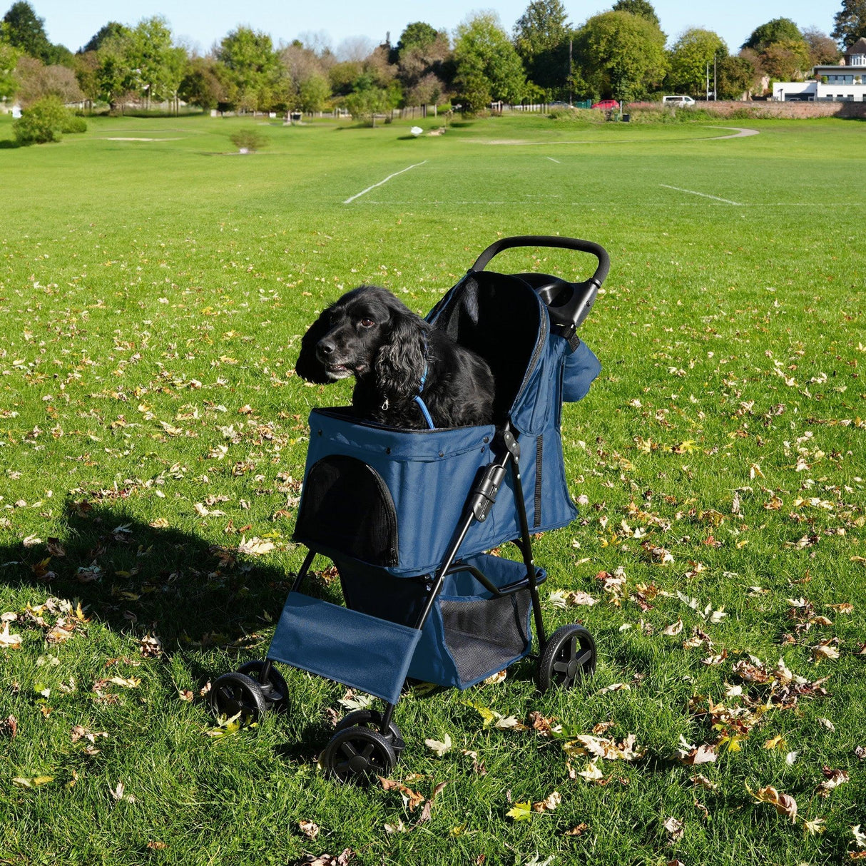Navy blue pet stroller with rain cover, featuring a spacious caddy bag and a happy black dog sitting comfortably inside on grass