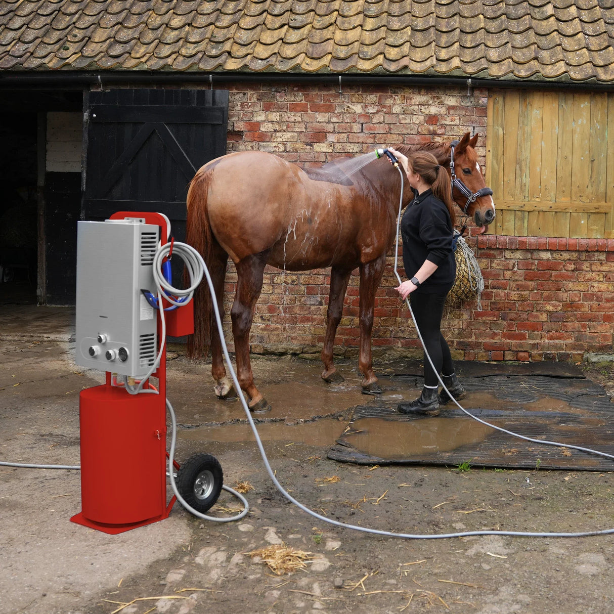 Deluxe portable horse shower in red, featuring a sleek design, hoses, and a user washing a horse in a rustic barn setting