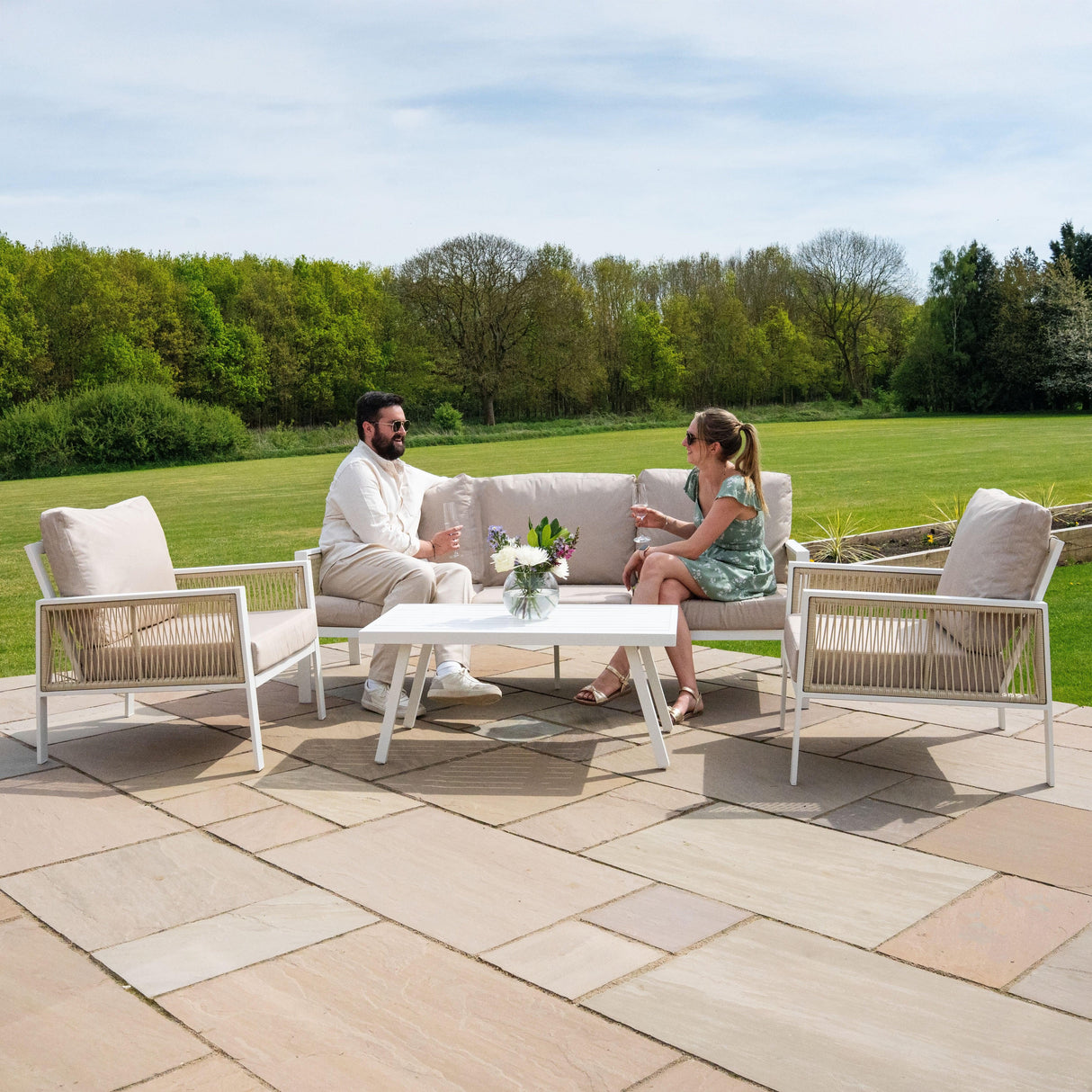 Aluminium 4 piece sofa set in white with plush beige cushions, featuring a modern design, placed on a patio with greenery in the background