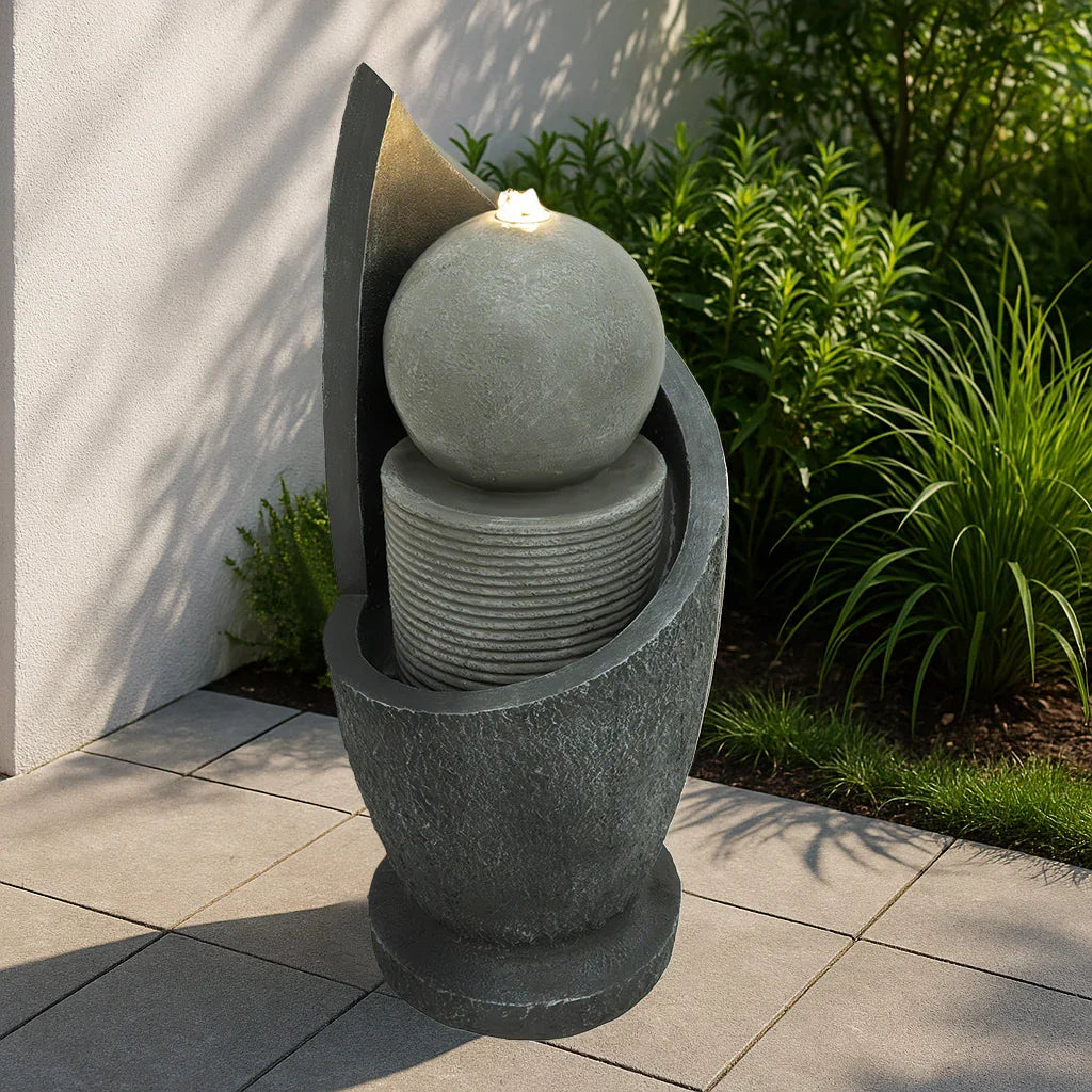 Zen Cascade electric water feature with a sleek dark stone finish, featuring a round top sphere and layered circular tiers, surrounded by greenery