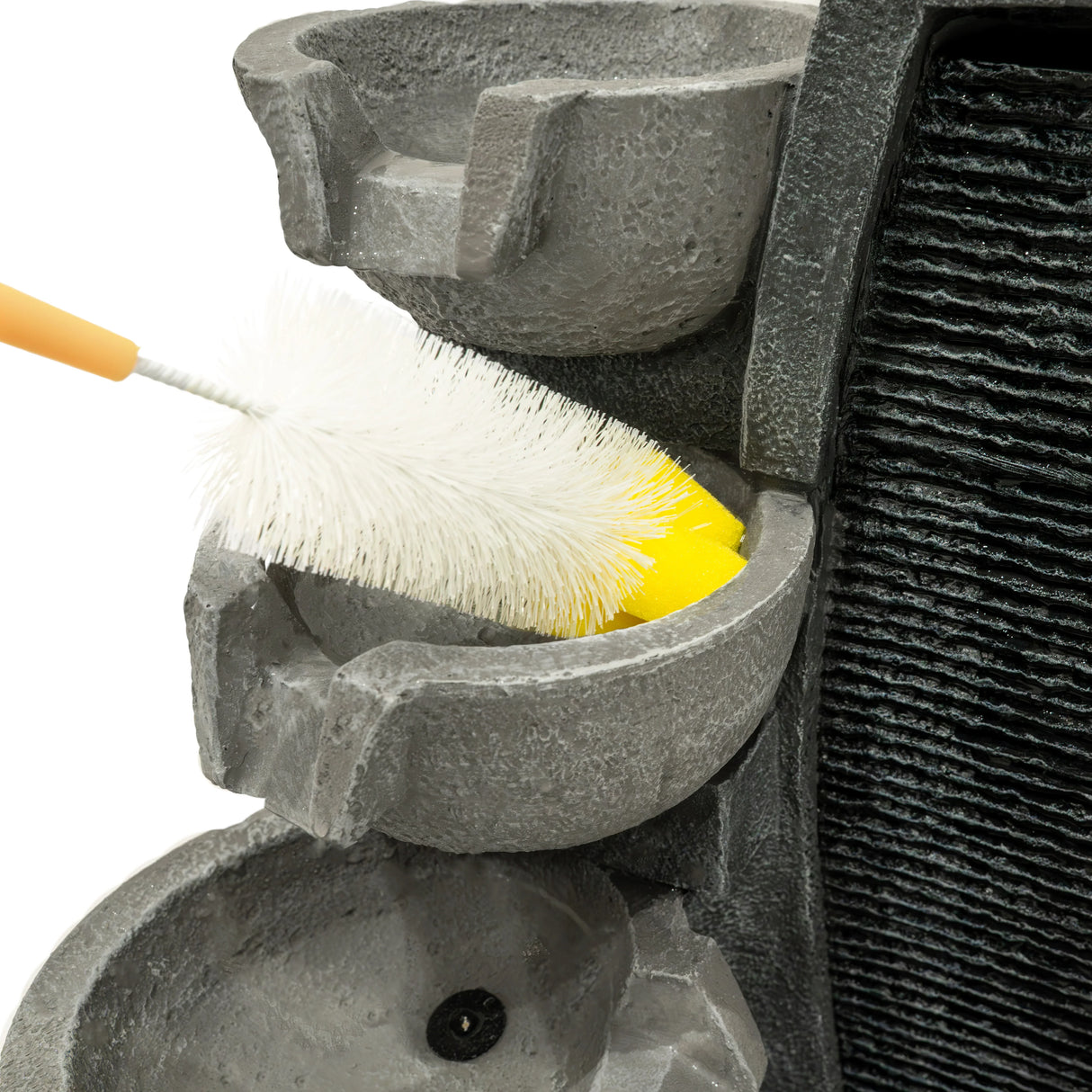 Cleaning brush reaching into one of the textured gray basins of the Sleek Streams electric water feature, showcasing its design and maintenance needs