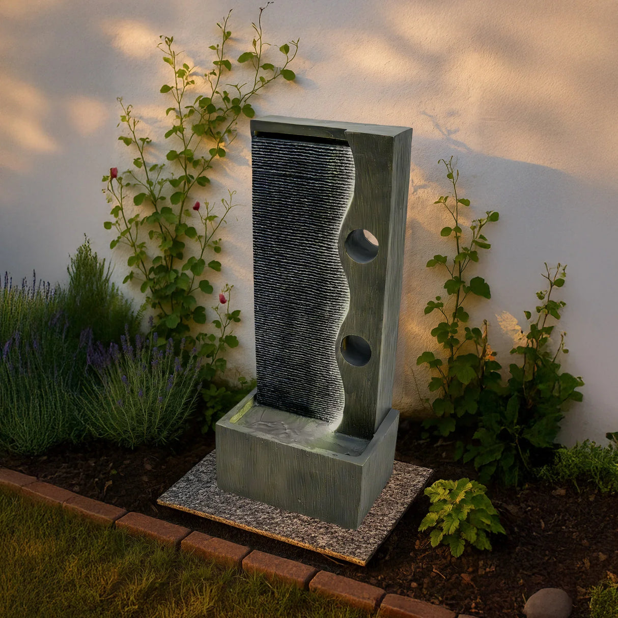 Electric water feature Harmony Falls with a sleek gray design, flowing water, and textured surface, surrounded by greenery and flowers