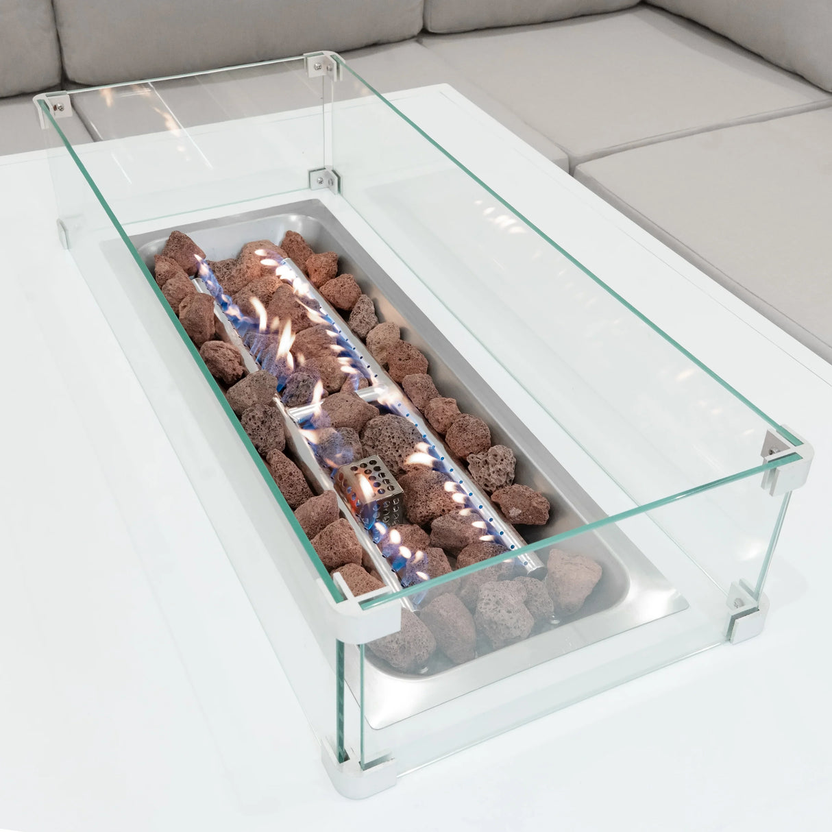 Modular garden furniture set featuring a sleek white fire pit with glass surround, glowing flames, and decorative lava rocks