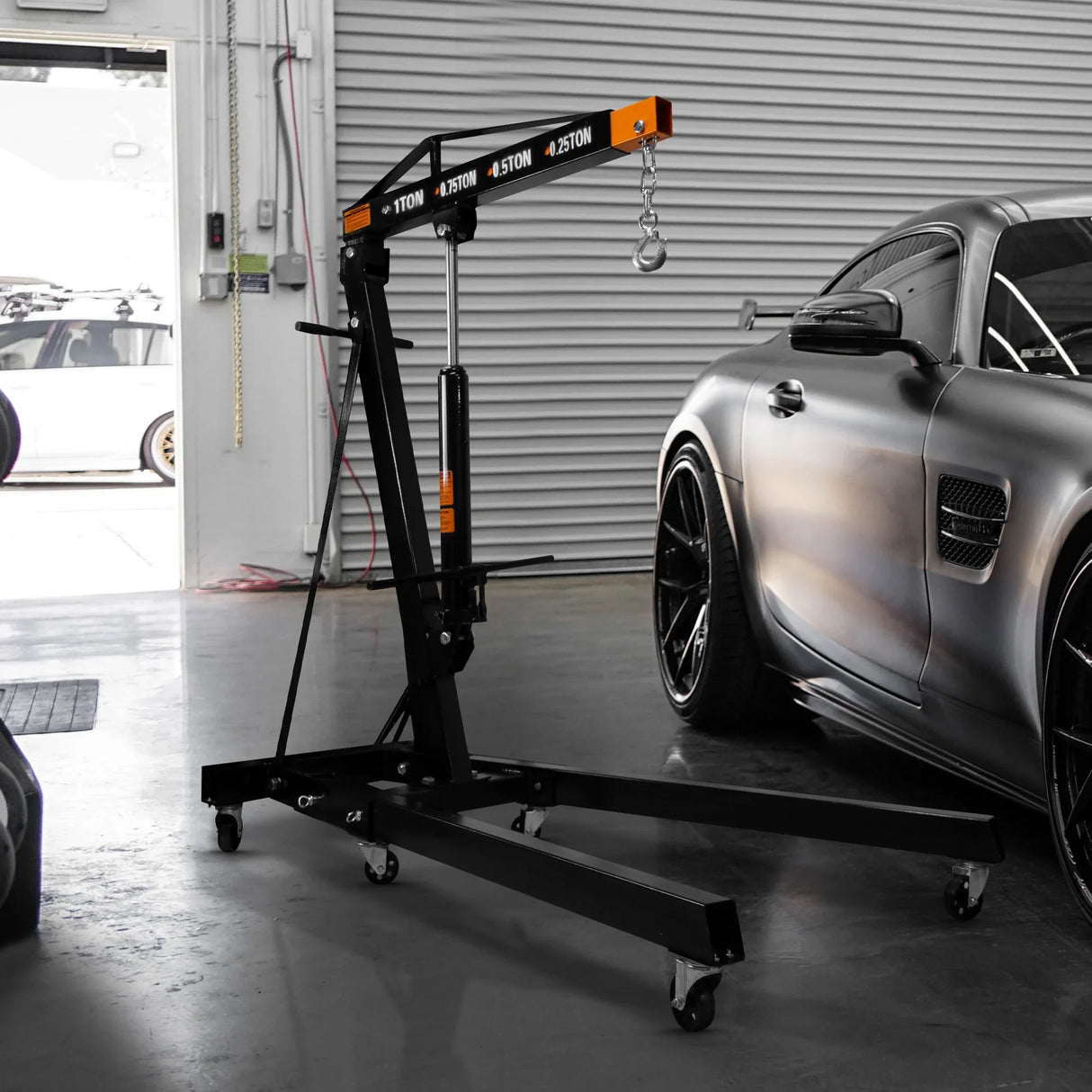 Heavy-duty black engine crane with load leveller, featuring a sturdy frame, wheels for mobility, and a sleek design beside a car
