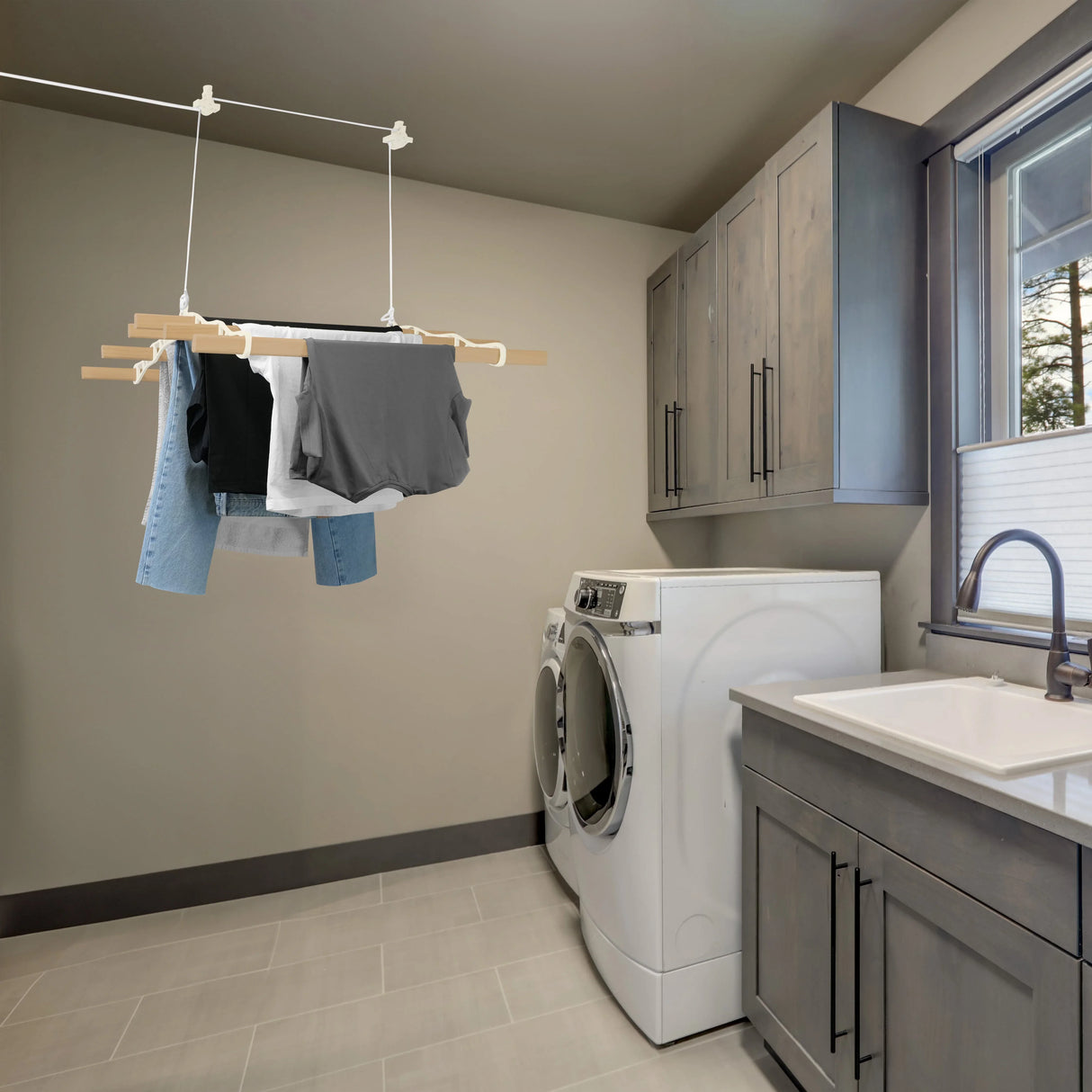 Ceiling pulley clothing airer in ivory, featuring wooden rods holding various garments, set in a modern laundry room with grey walls