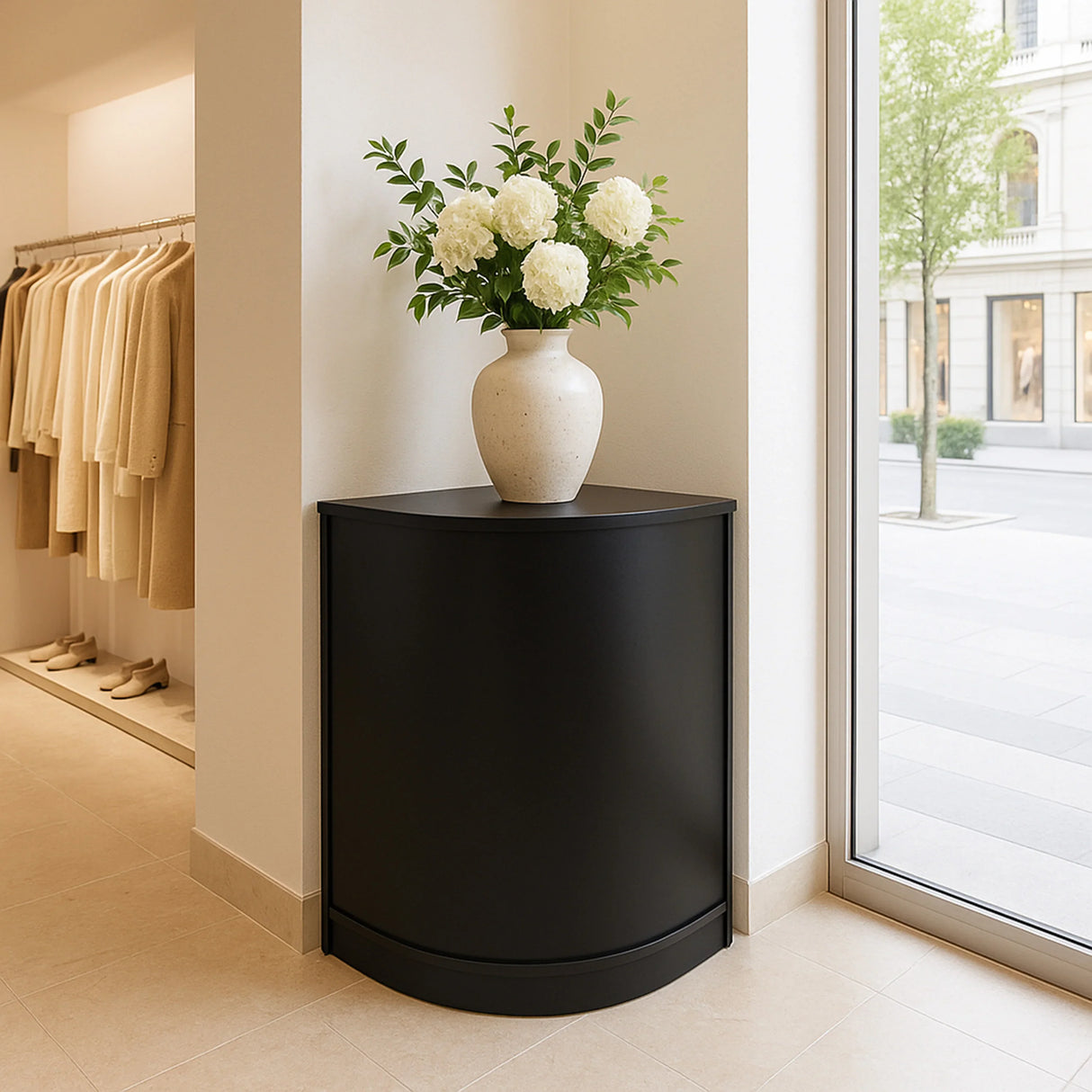 Sleek black retail shop corner counter CM60 with a rounded design, topped with a vase of white flowers, enhancing a modern space