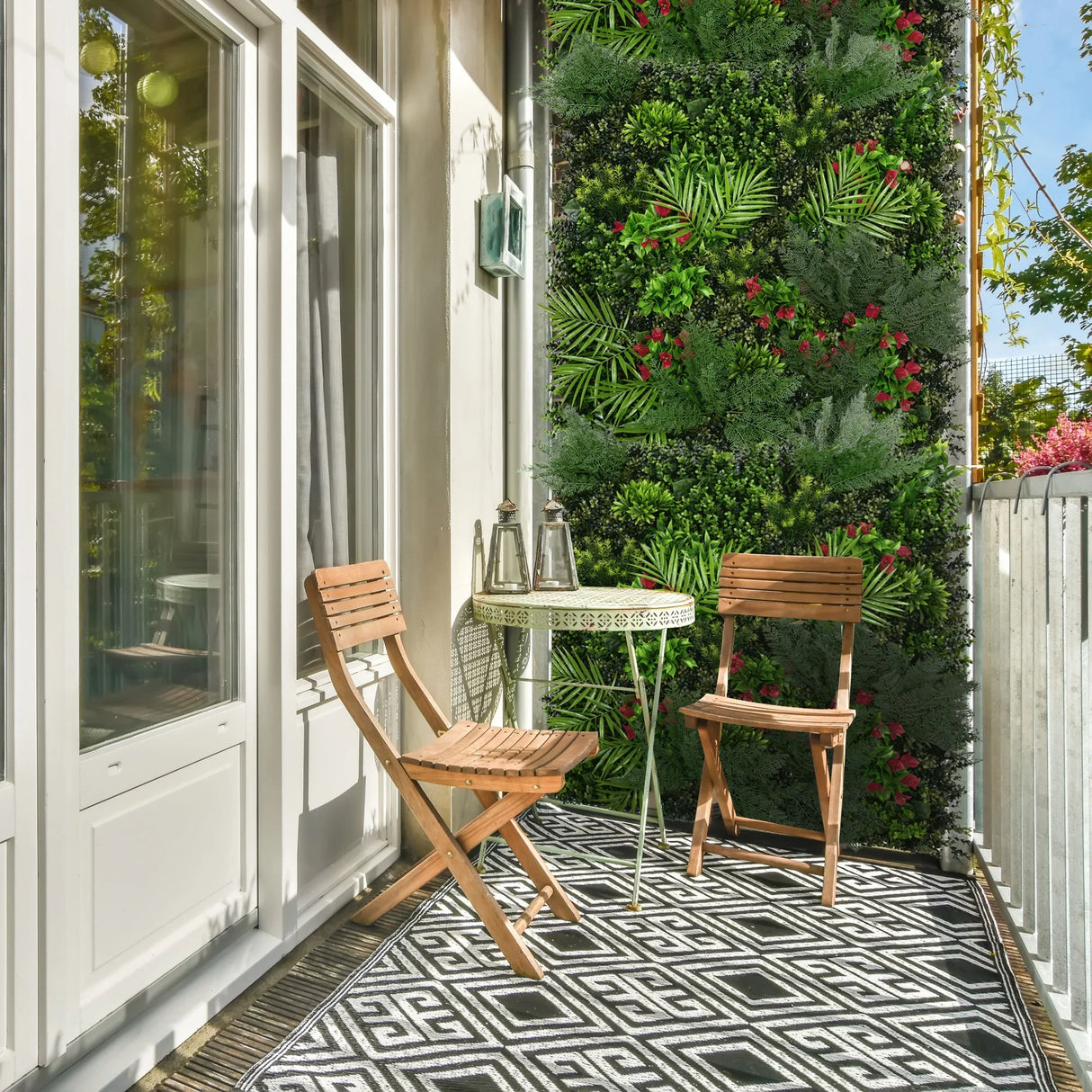 Mira Artificial Wall Tile in lush green with vibrant flowers, enhancing a stylish balcony with wooden chairs and a round table