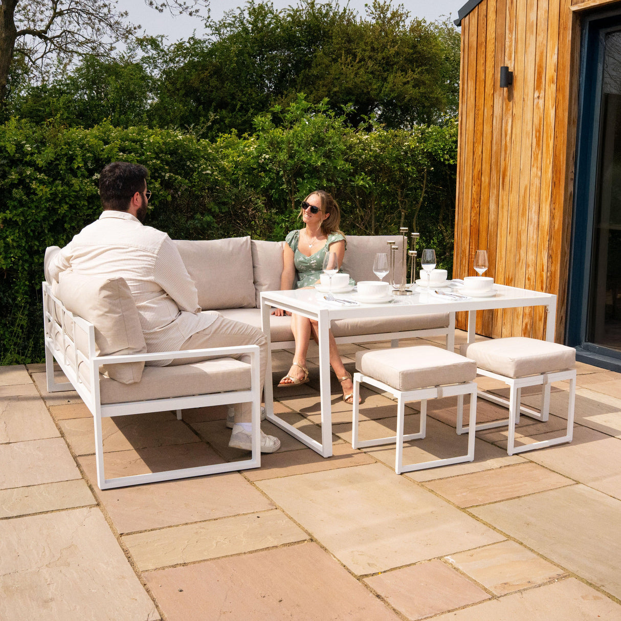 Stylish white aluminium corner sofa set with plush cushions, paired with a modern dining table and stools, perfect for outdoor lounging