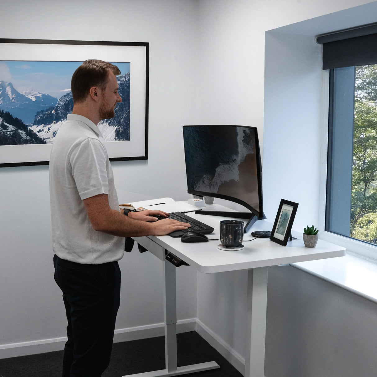 Electric standing desk with drawer, sleek white finish, adjustable height, modern design, paired with a monitor and accessories in a bright office setting