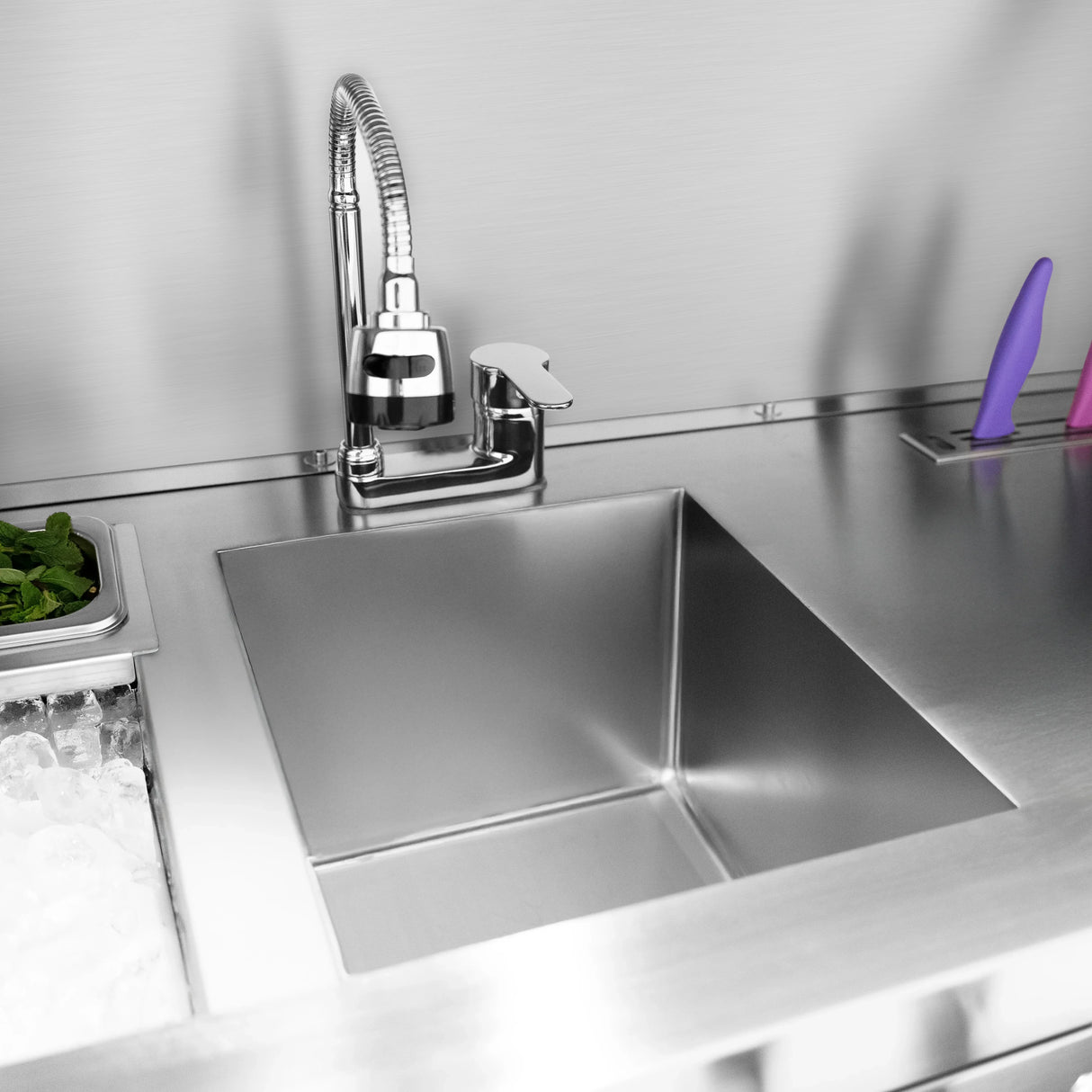Stainless steel sink with a sleek faucet, surrounded by ice, fresh mint, and colorful cocktail tools on a mobile bar station