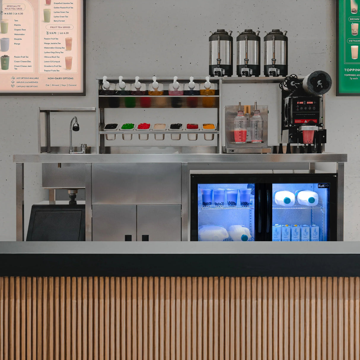 Complete bubble tea workstation with stainless steel counter, colorful ingredient dispensers, and a glass-front fridge showcasing drinks