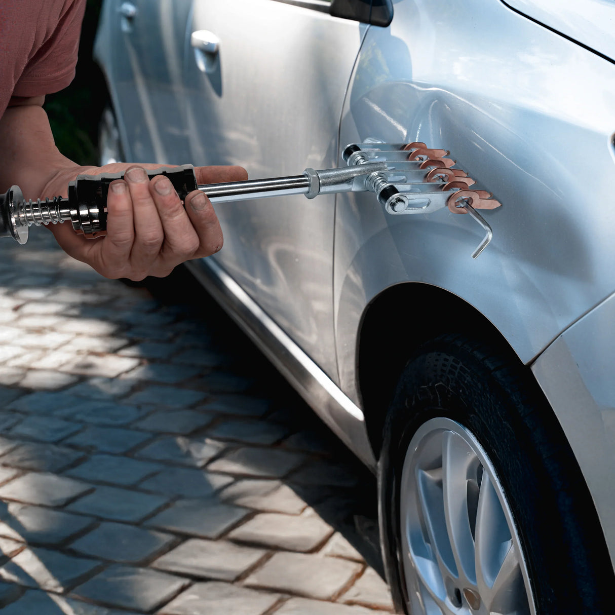 Dent puller machine in use, featuring a metal handle, multiple copper tabs, and a sleek silver car body with a visible dent