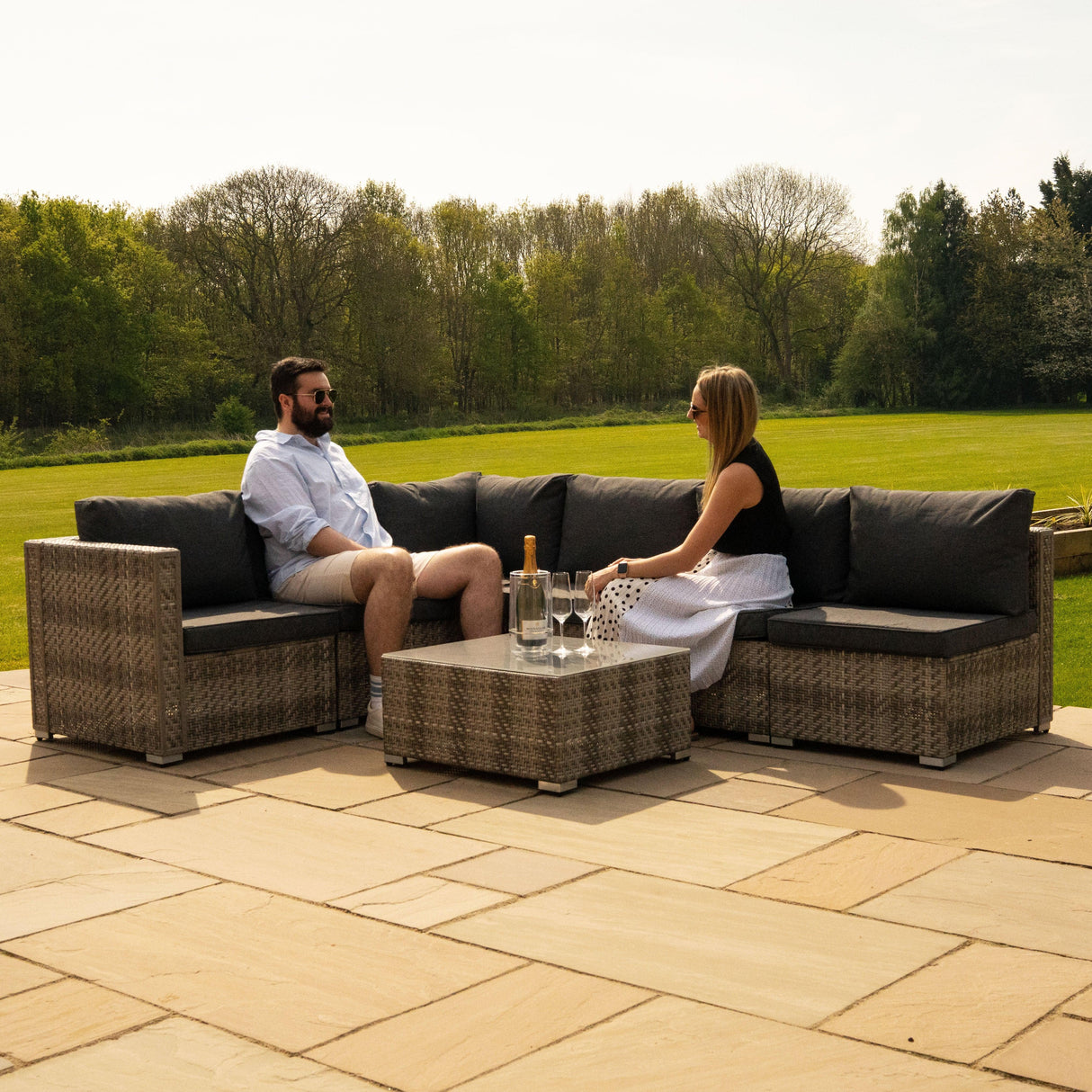 Rattan modular 7 piece furniture set in grey with plush cushions, arranged on a patio, featuring two seated individuals enjoying the outdoors