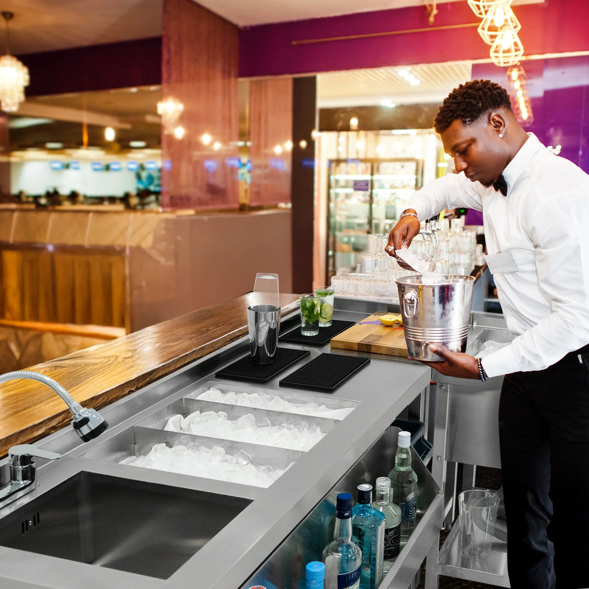 Modular cocktail bar station with ice well, sleek stainless steel design, bartender preparing drinks, vibrant bar atmosphere