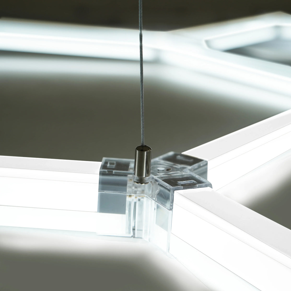 Hexagon LED lighting fixture with a sleek, transparent frame and a metallic suspension cable, showcasing modern design and bright illumination
