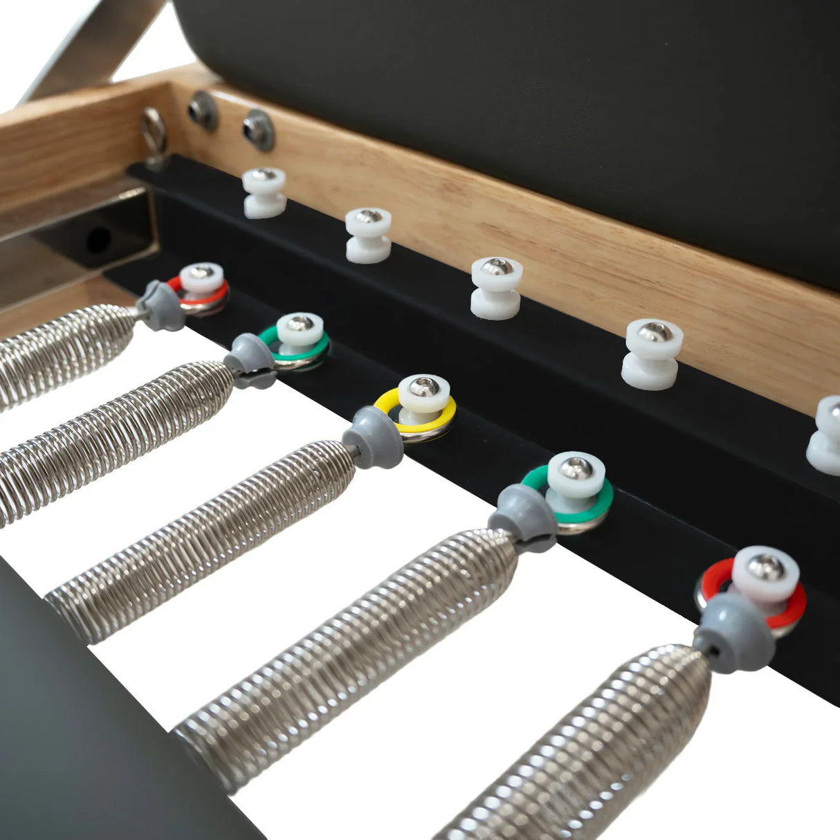 Close-up of the Pilates reformer machine in oak, showcasing the springs, adjustable settings, and sleek black upholstery