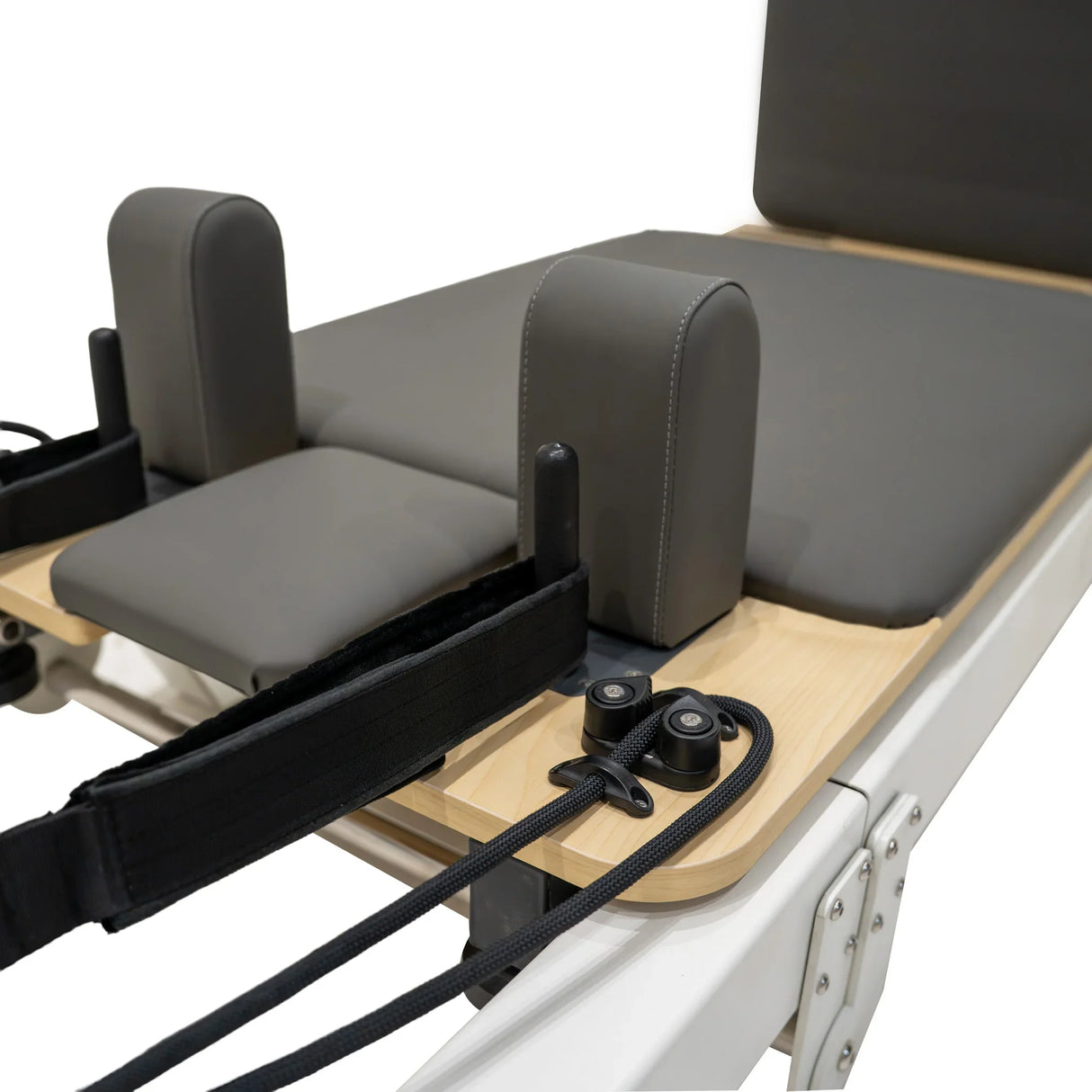 Aluminium Pilates reformer machine featuring a padded gray platform, adjustable straps, and sturdy wooden frame for stability
