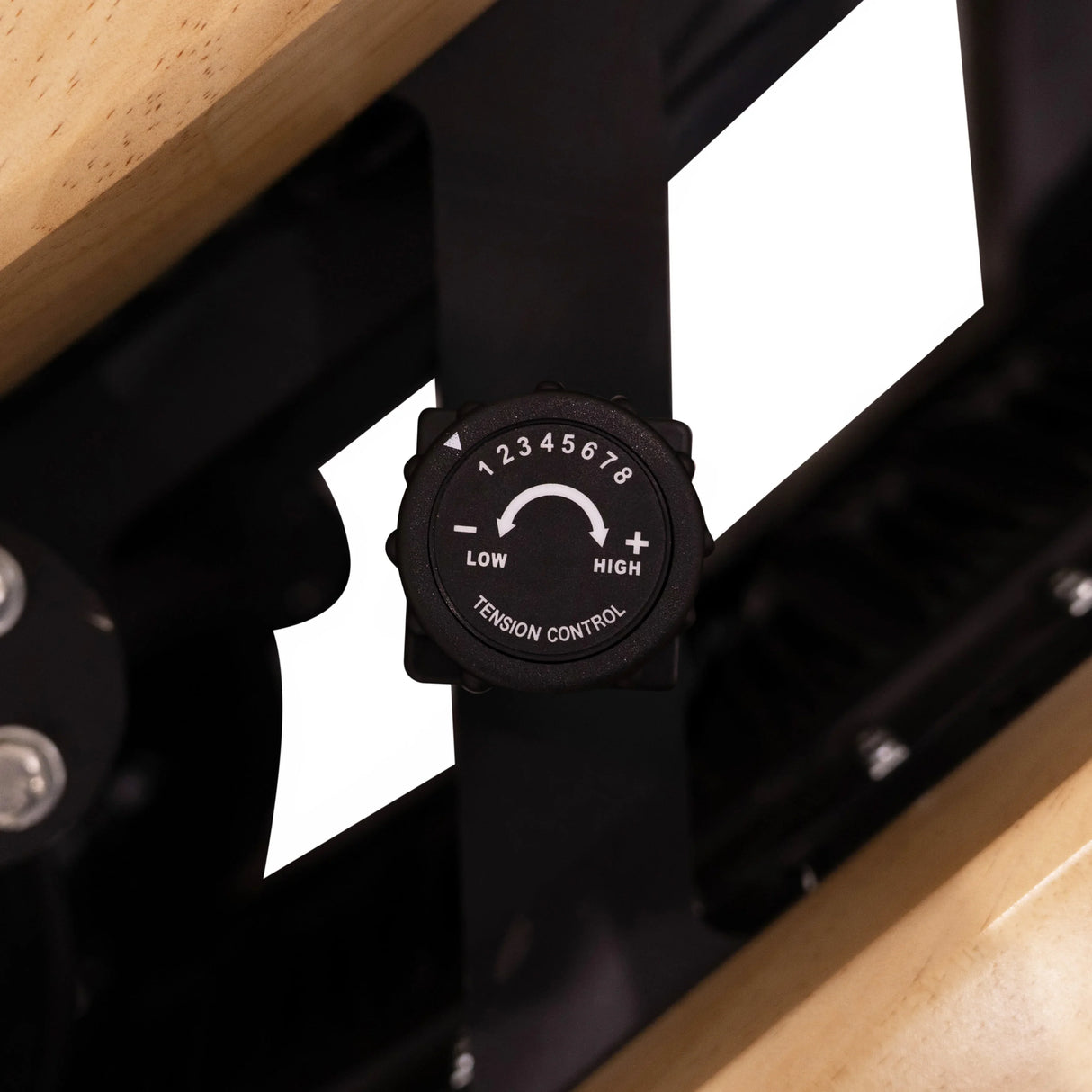 Curved treadmill tension control knob in black, featuring low and high settings, set against a light oak frame background
