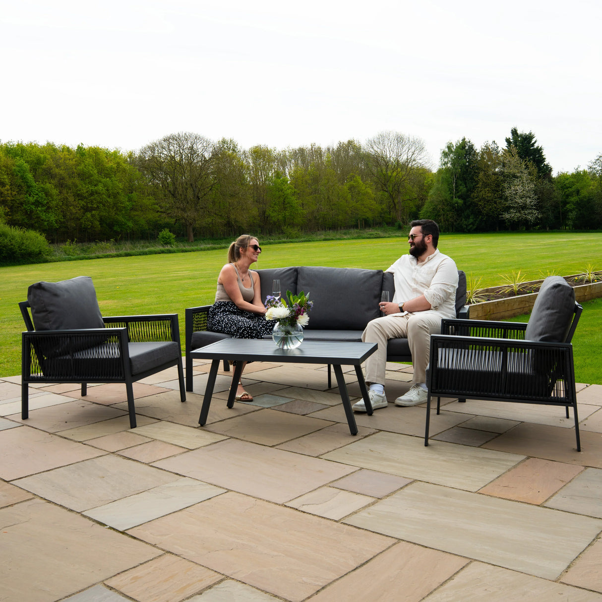 Anthracite grey aluminium 4-piece sofa set with plush cushions, stylish black rattan storage box, set on a patio with greenery in the background