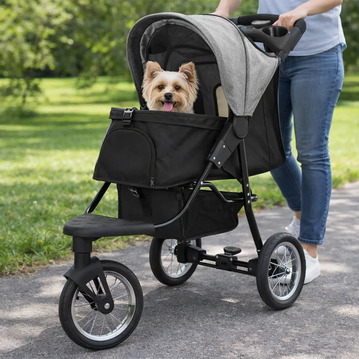 Grey pet jogger with a cozy canopy, featuring a happy small dog inside, rolling on a path surrounded by greenery